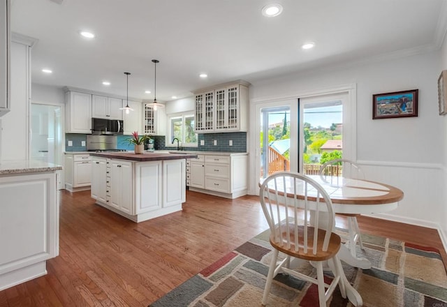 kitchen with a center island, stainless steel microwave, wood finished floors, tasteful backsplash, and glass insert cabinets