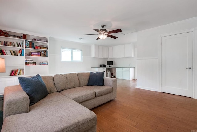 living area featuring light wood-style floors, a wainscoted wall, ceiling fan, and ornamental molding