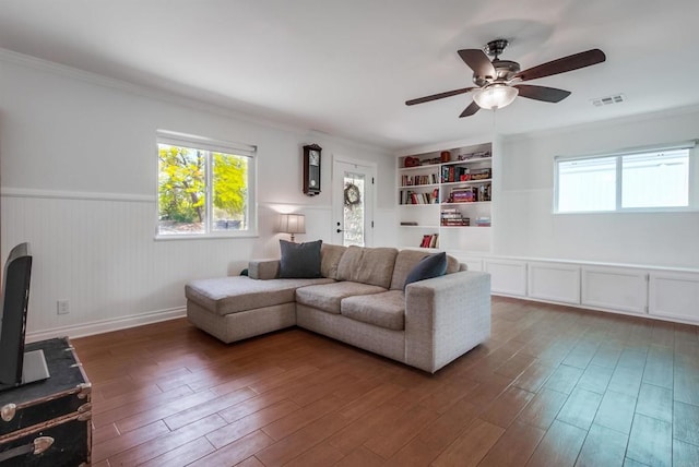 living room featuring a wainscoted wall, a ceiling fan, wood finished floors, visible vents, and ornamental molding