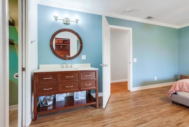 bathroom featuring vanity, baseboards, wood finished floors, visible vents, and ornamental molding