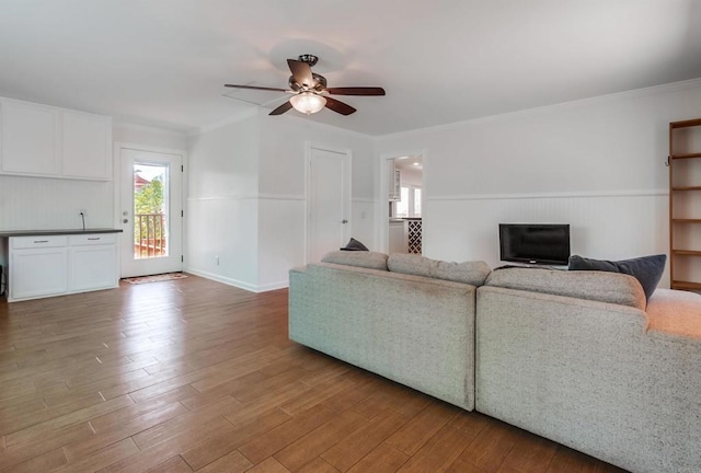 living room featuring a ceiling fan, ornamental molding, wood finished floors, and a wainscoted wall