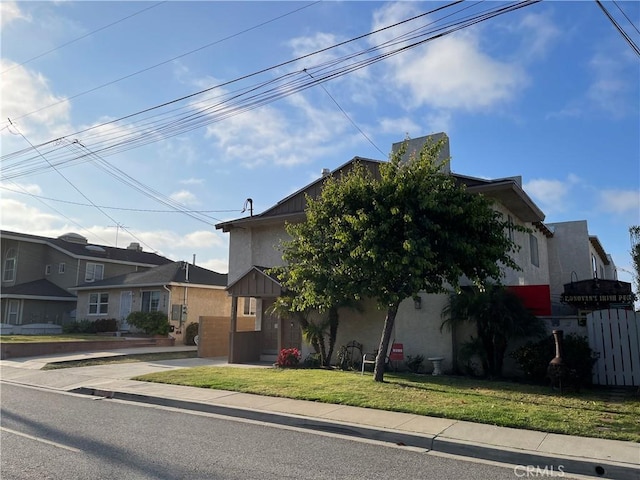 view of property hidden behind natural elements featuring a residential view, a front lawn, and stucco siding