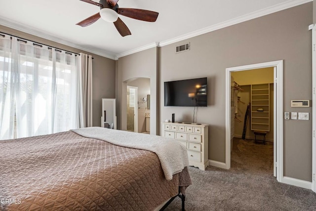 carpeted bedroom featuring a walk in closet, visible vents, arched walkways, baseboards, and ornamental molding