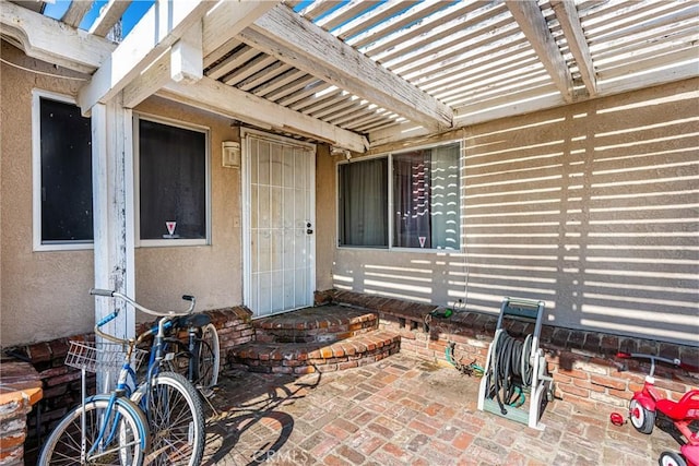 property entrance with a patio area, stucco siding, and a pergola