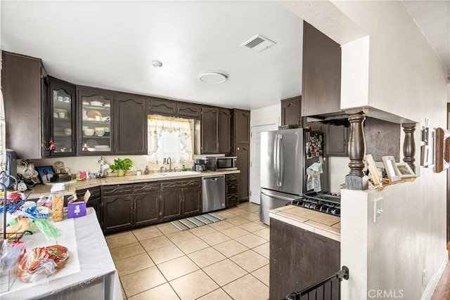 kitchen featuring dark brown cabinetry, visible vents, a sink, light tile patterned floors, and stainless steel appliances