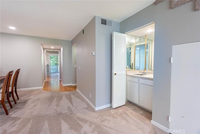 hallway with a sink, baseboards, light colored carpet, and visible vents