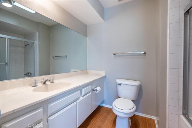 bathroom with a tile shower, vanity, toilet, baseboards, and wood finished floors