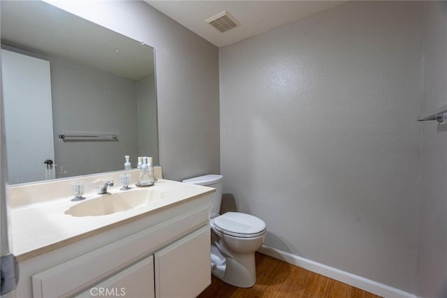 bathroom with vanity, toilet, baseboards, wood finished floors, and visible vents