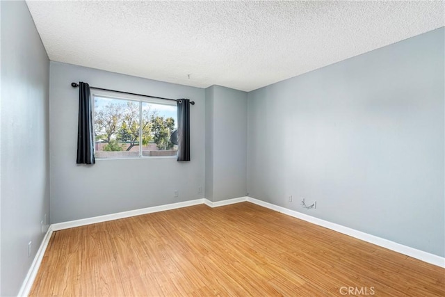 empty room with a textured ceiling, baseboards, and wood finished floors