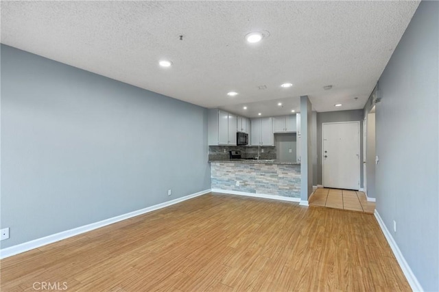 unfurnished living room featuring recessed lighting, baseboards, light wood finished floors, and a textured ceiling