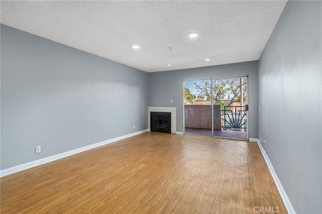 unfurnished living room featuring a fireplace, a textured ceiling, light wood-style flooring, recessed lighting, and baseboards