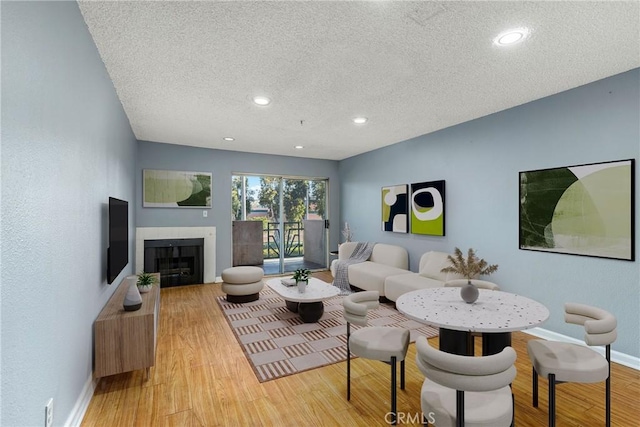 living area featuring a textured ceiling, a fireplace, light wood-type flooring, baseboards, and recessed lighting