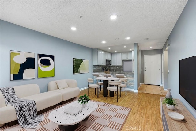 living area with light wood-style floors, recessed lighting, a textured ceiling, and baseboards