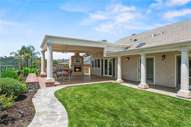 back of house featuring fence, a patio, stucco siding, a lawn, and a lit fireplace