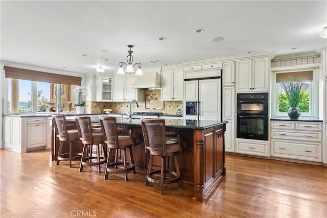 kitchen featuring dobule oven black, tasteful backsplash, wood finished floors, a breakfast bar, and an island with sink