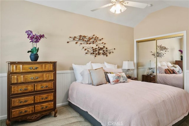carpeted bedroom with a closet, ceiling fan, a wainscoted wall, and vaulted ceiling