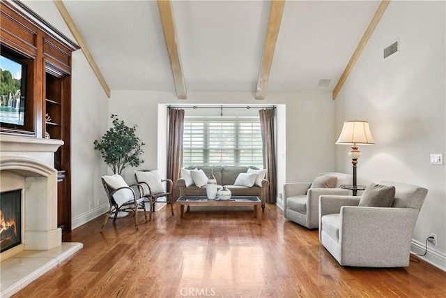 living area featuring wood finished floors, a premium fireplace, beam ceiling, and visible vents