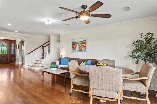 dining area with arched walkways, a ceiling fan, wood finished floors, visible vents, and ornamental molding