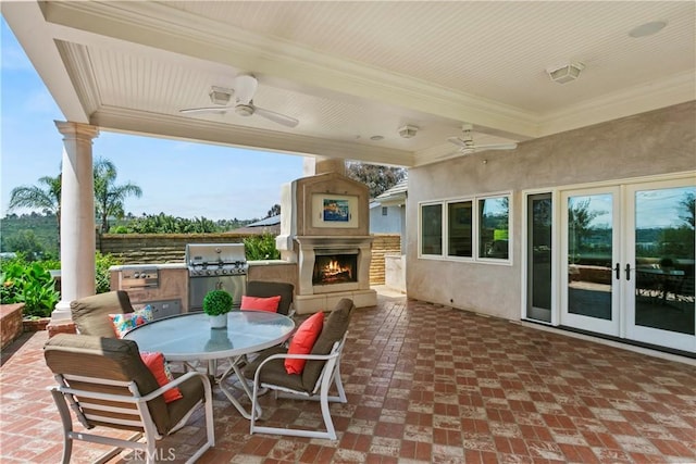 view of patio / terrace with french doors, ceiling fan, exterior kitchen, and a lit fireplace