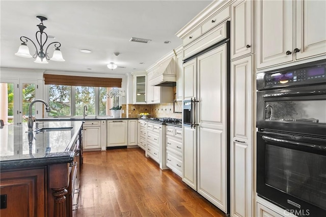 kitchen with decorative backsplash, paneled appliances, custom range hood, a sink, and dark stone countertops