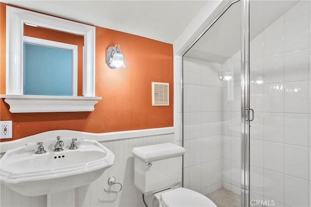 bathroom with a sink, toilet, a wainscoted wall, a shower stall, and visible vents