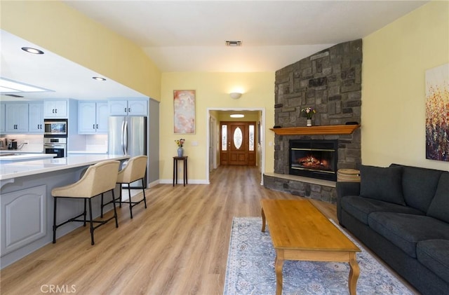 living room featuring a stone fireplace, light wood-style floors, baseboards, and recessed lighting