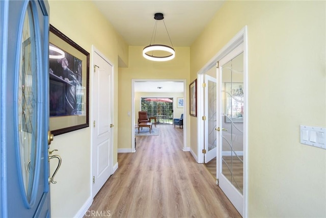hall with light wood-type flooring, baseboards, and french doors