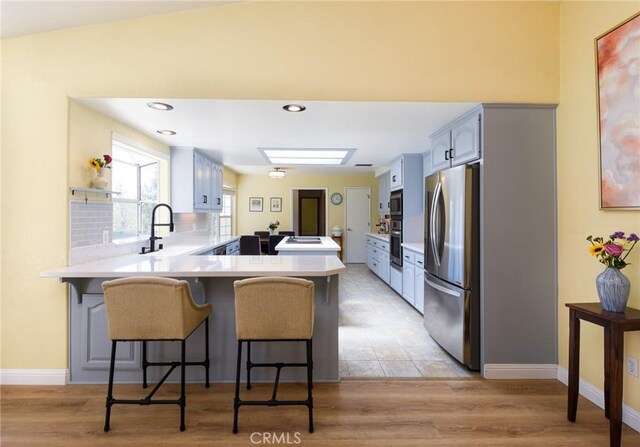 kitchen with appliances with stainless steel finishes, a peninsula, a breakfast bar area, light countertops, and recessed lighting