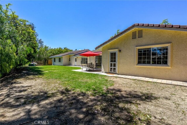 rear view of property with stucco siding, a patio, and a yard