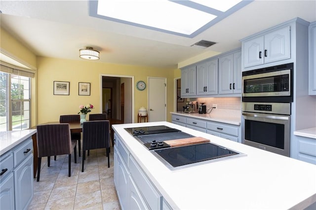 kitchen with appliances with stainless steel finishes, decorative backsplash, light countertops, light stone finish floors, and gray cabinetry