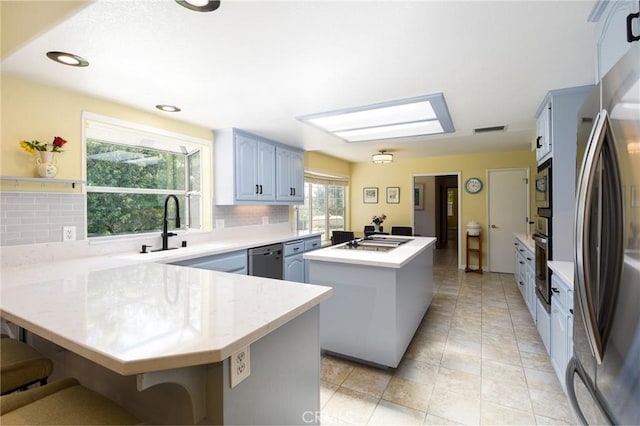 kitchen featuring stainless steel appliances, a peninsula, a center island, decorative backsplash, and a kitchen breakfast bar