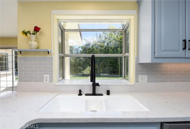 kitchen view of a sink, decorative backsplash, open shelves, and light stone countertops