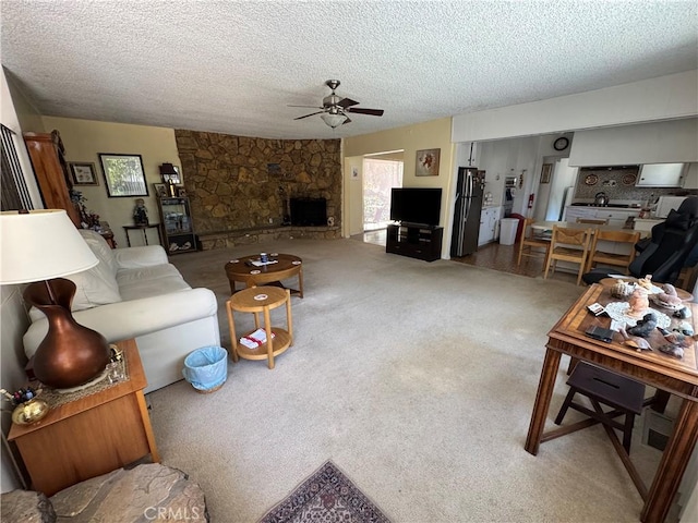 carpeted living room featuring a textured ceiling, ceiling fan, and a stone fireplace
