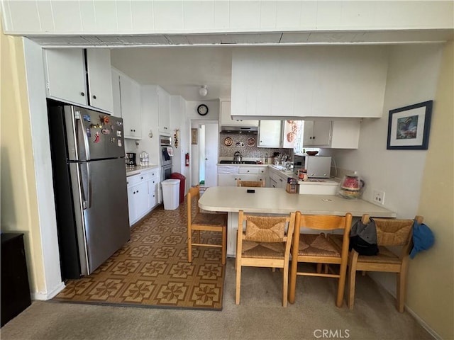 kitchen with white cabinets, appliances with stainless steel finishes, light countertops, a peninsula, and tasteful backsplash