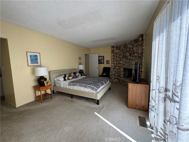 carpeted bedroom featuring a stone fireplace, a textured ceiling, and visible vents