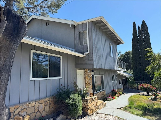 tri-level home featuring board and batten siding, a balcony, and stone siding