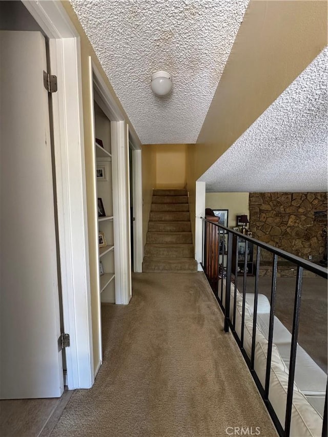 hallway featuring carpet flooring, a textured ceiling, built in features, and stairway