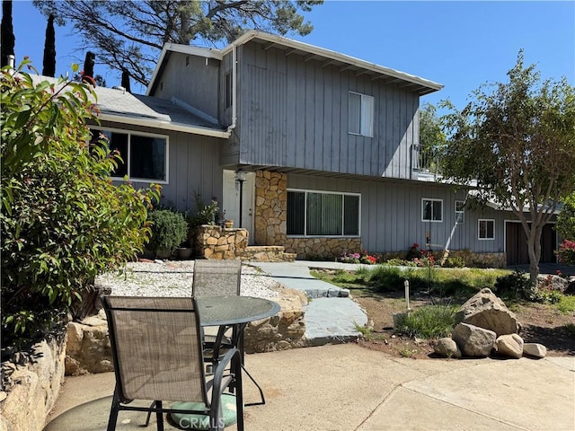 rear view of property featuring board and batten siding, a patio, outdoor dining area, and stone siding