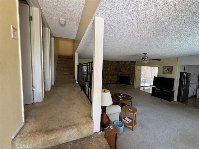 stairs with a stone fireplace, carpet flooring, a textured ceiling, and a ceiling fan