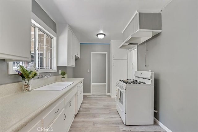 9451 Canterbury Ave, Arleta, CA 91331 - kitchen with white gas stove, a sink, light wood-style floors, baseboards, and white cabinets