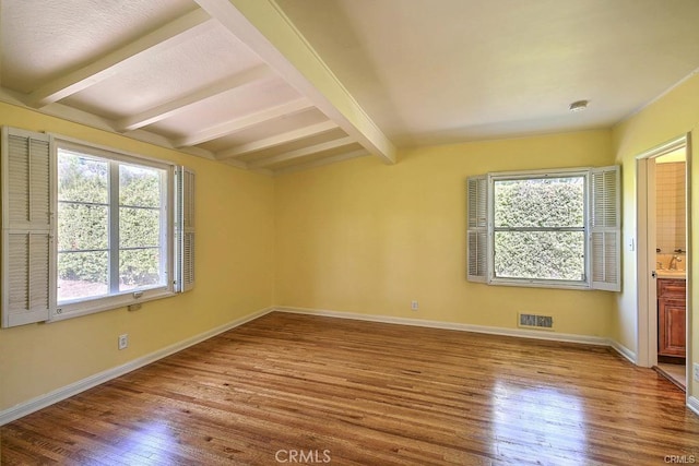 empty room featuring visible vents, lofted ceiling with beams, baseboards, and wood finished floors