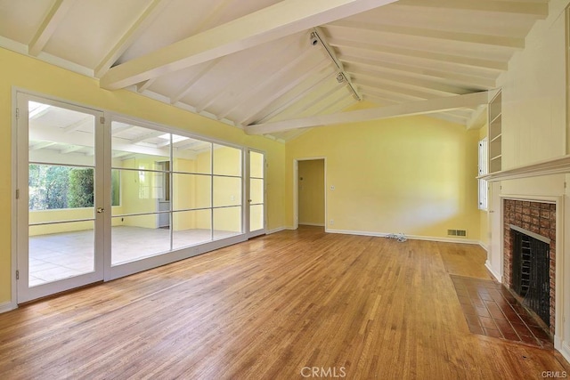 unfurnished living room with track lighting, a tiled fireplace, vaulted ceiling with beams, wood finished floors, and visible vents