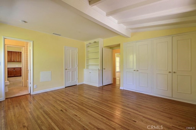 unfurnished bedroom with lofted ceiling with beams, ensuite bath, baseboards, wood finished floors, and visible vents