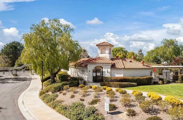 view of front of property with stucco siding, a tile roof, a chimney, fence, and a gate