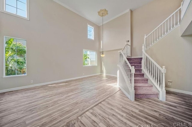 stairway with a high ceiling, wood finished floors, crown molding, and baseboards