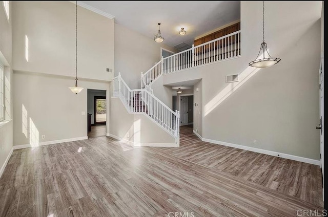 unfurnished living room featuring stairway, a high ceiling, wood finished floors, and baseboards