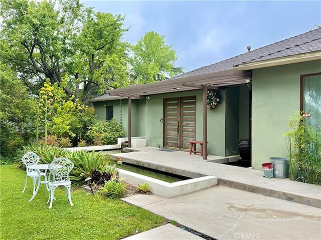 rear view of property featuring roof with shingles, stucco siding, and a yard
