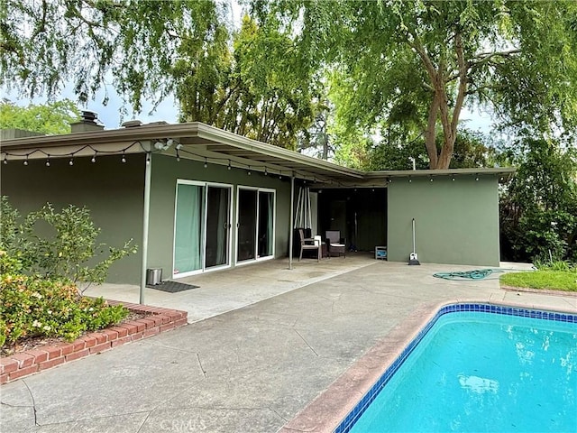 rear view of house featuring a patio, an outdoor pool, stucco siding, and a chimney