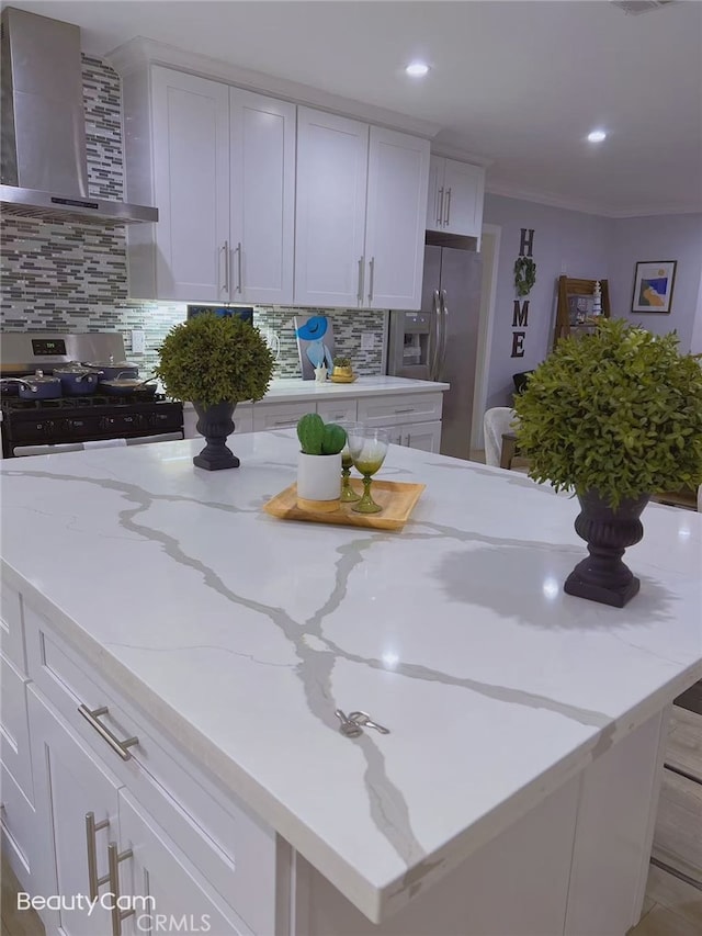 kitchen with decorative backsplash, stainless steel appliances, white cabinetry, and wall chimney exhaust hood