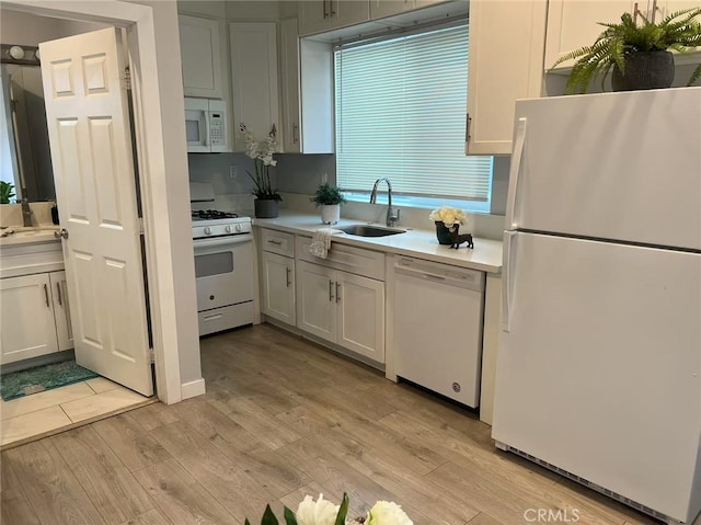 kitchen featuring white cabinets, a sink, light wood-style floors, white appliances, and light countertops